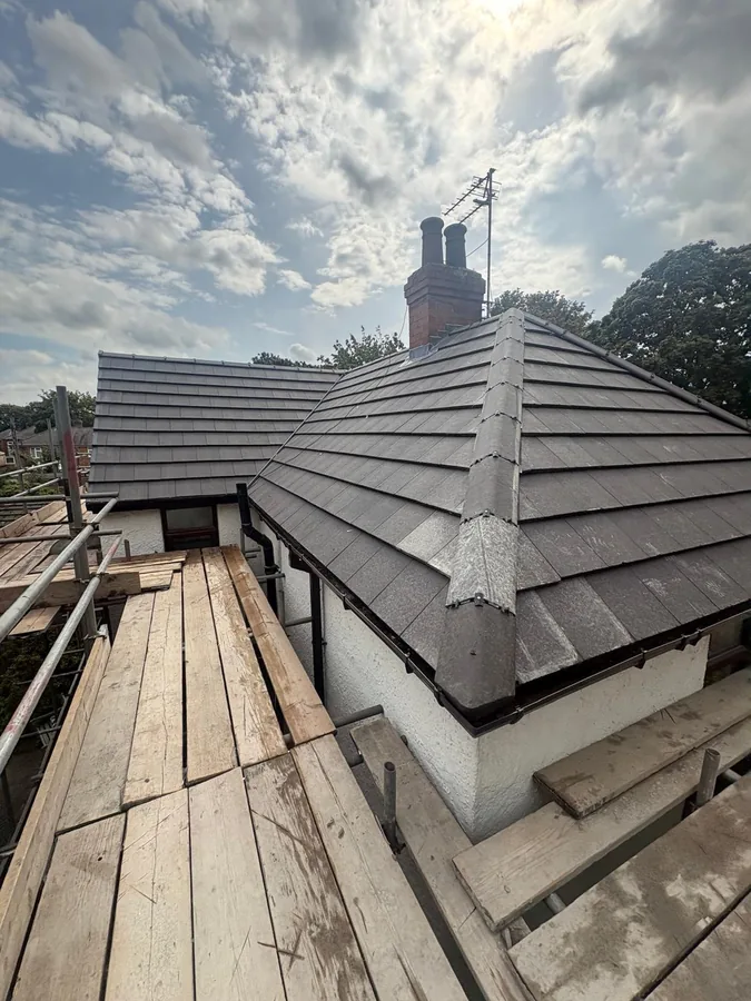 Completed grey flat tile hipped roof and chimney in Beverley under a broken cloudy sky