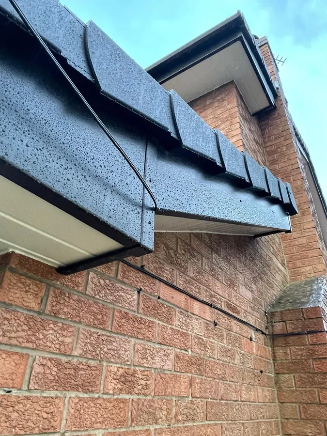 Anthracite grey dry verge units and black guttering on the gable of a red brick house